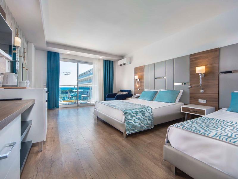 Chambre d'hôtel moderne avec lit double et simple, sol en bois et balcon avec vue sur la mer.