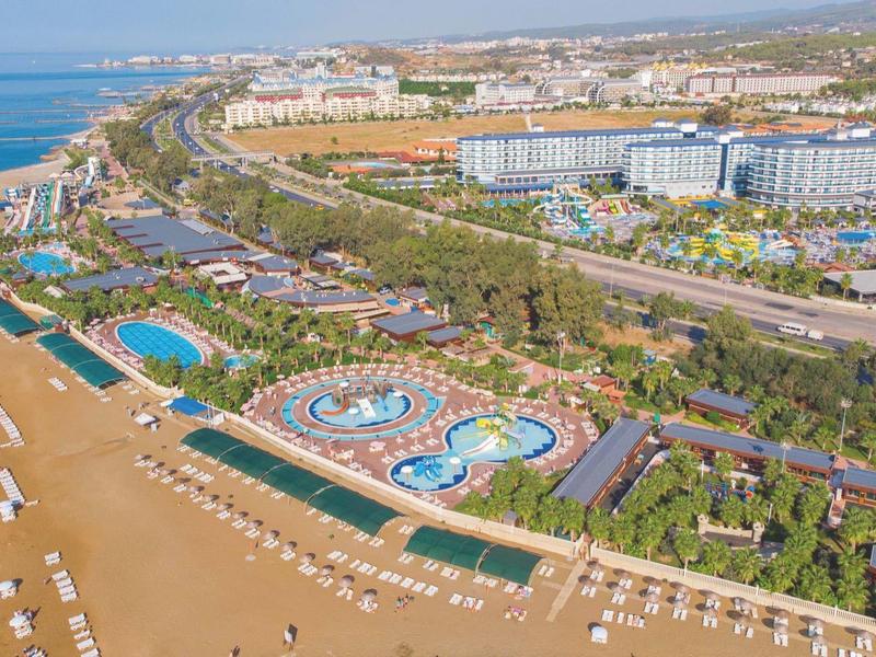 Vue aérienne d'un complexe de plage de villégiature avec piscines, bâtiments et zone de plage le long de la côte.
