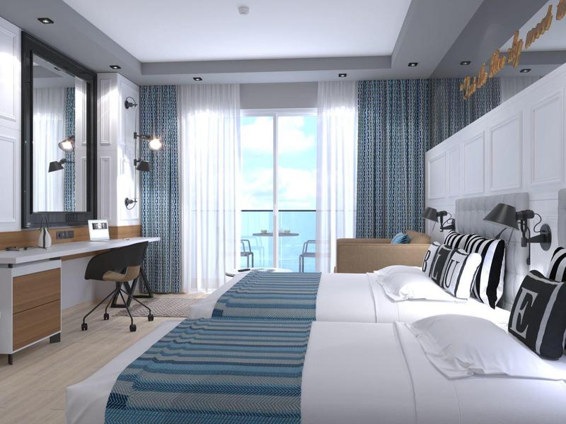 Chambre d'hôtel moderne avec deux lits, espace de travail et balcon avec vue sur la mer.