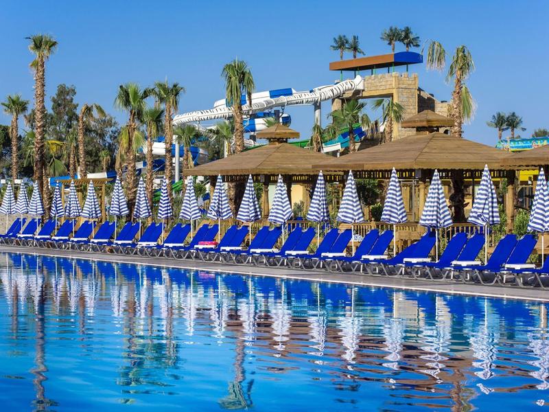 Piscine longue avec chaises longues bleues et parasols rayés dans une station ensoleillée.