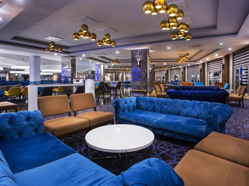 Salon d'hôtel moderne avec canapés bleus et marron et tables rondes sous des lampes dorées.