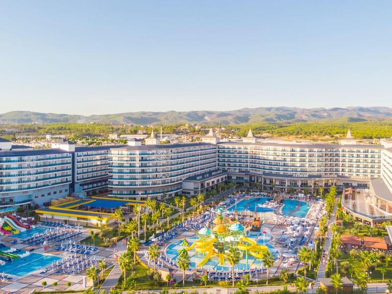 Grand complexe hôtelier avec plusieurs piscines, toboggans aquatiques et montagnes en arrière-plan.