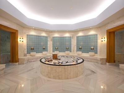 Großer Hamam mit Marmor, runder zentraler Ablage und blauen Fliesen an den Wänden.