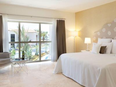 Helles Schlafzimmer mit großem Bett, Polsterkopfteil, zwei Nachttischlampen und Balkon mit Glasfront.