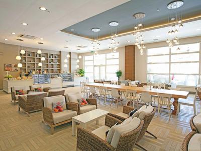 Helles Café mit Holzmobiliar, großen Fenstern, Sitzgruppen und langem Tisch mit Stühlen.