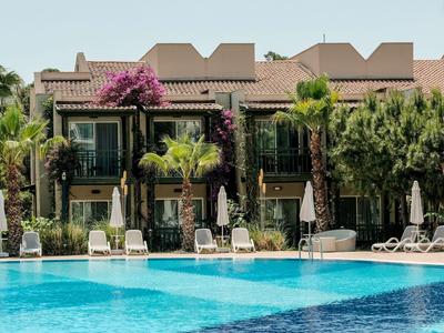 A hotel with blooming plants, sun loungers, and a large clear pool in the foreground.