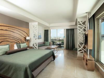 Modern hotel room with large bed, balcony, and sea view in daylight.