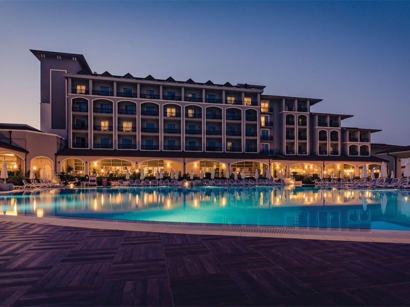 Een groot hotel met een verlicht buitenzwembad bij schemering en een heldere lucht.