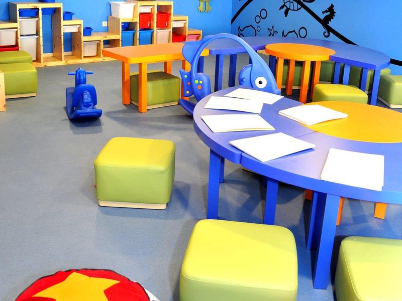 Kleurrijke, speelse kinderhoek met speelgoed, tafels, krukjes en oceaanthema aan de muur.