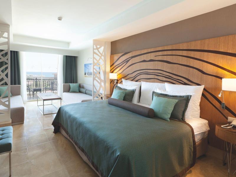 Lichte hotelkamer met groot bed, elegante houten hoofdbord en balkon met uitzicht naar buiten.