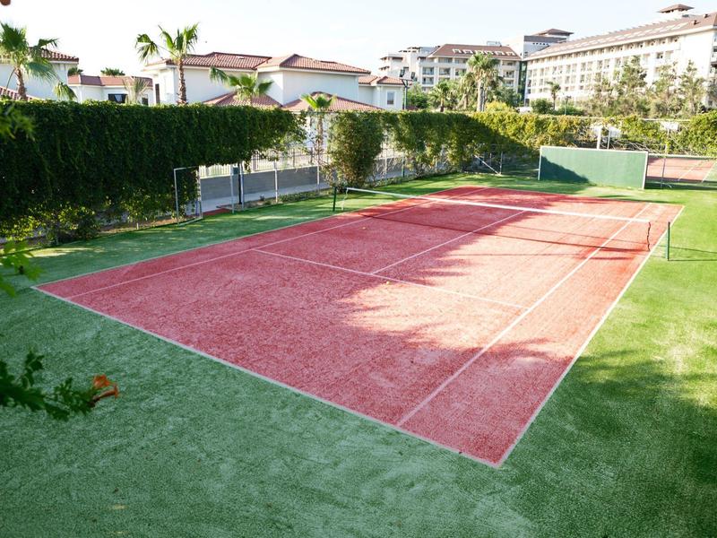 Buiten tennisbaan met kunstgras en roodgroen oppervlak nabij hotelgebouwen.