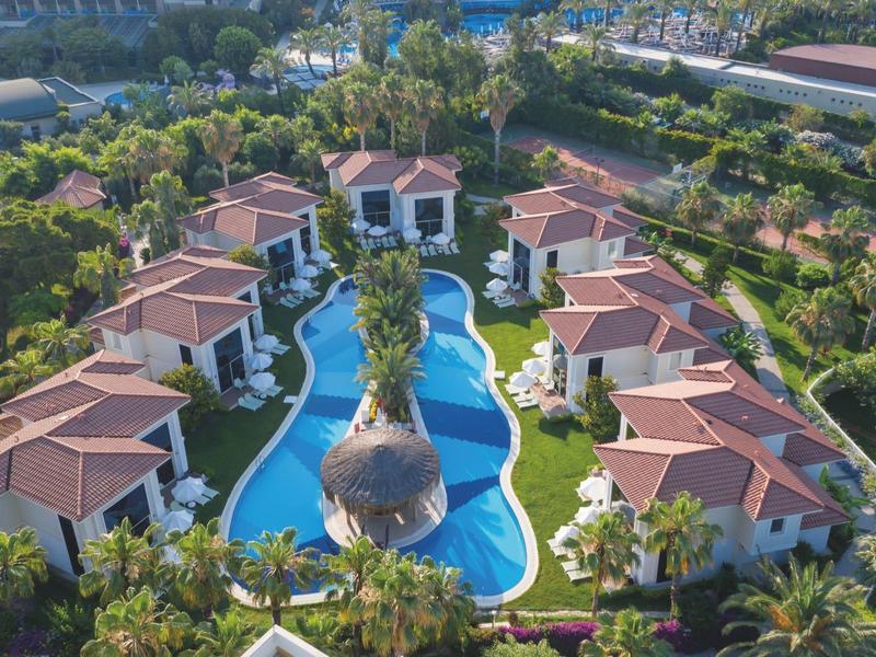 Luchtbeeld van een tropisch resort met villa's rond een kronkelend zwembad en weelderig groen.