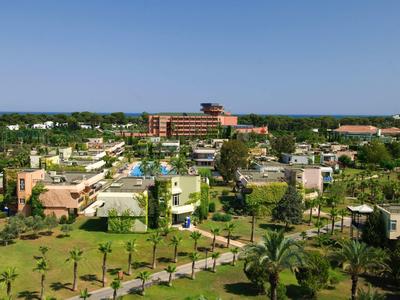 Pohled na hotelový resort se zelenými zahradami, bazény a vícepatrovými budovami pod jasnou oblohou.