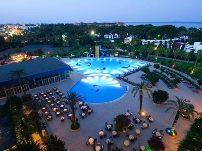 Vista notturna di una piscina illuminata in un resort con tavoli e palme