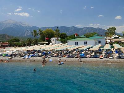 Spiaggia con ombrelloni e persone al mare azzurro chiaro con montagne sullo sfondo.