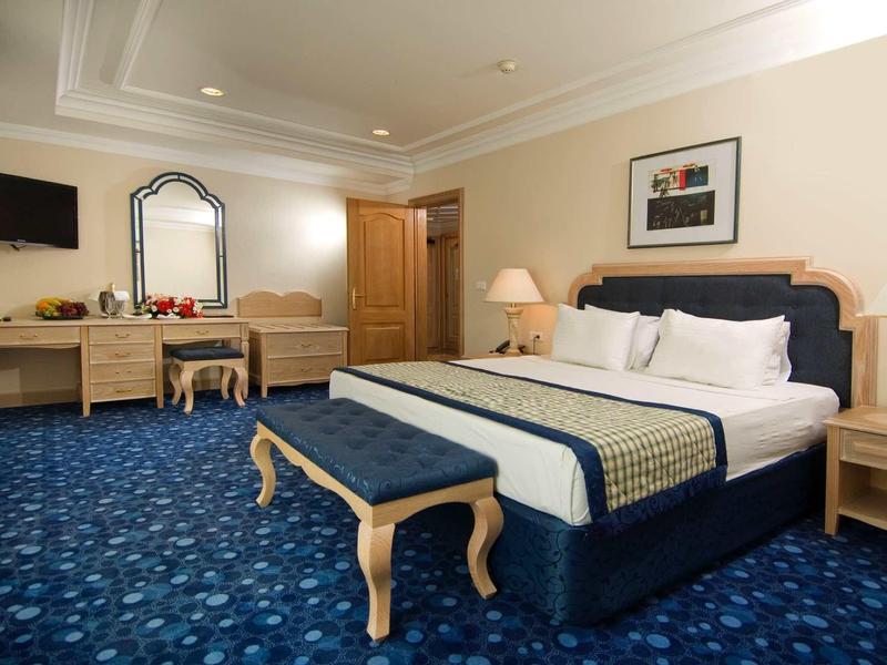 Elegantní hotelový pokoj s velkou postelí, modrým kobercem a dřevěným nábytkem.