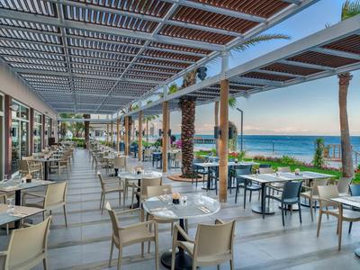 Offenes Restaurant mit modernen Tischen, Stühlen, Palmen und Meerblick bei Sonnenuntergang.