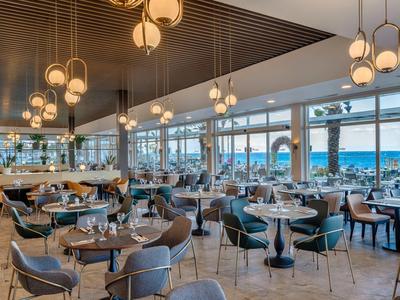 Ristorante di hotel elegante con mobili moderni e vista sull'acqua attraverso grandi finestre.