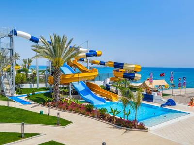 Parco scivoli d'acqua colorato vicino alla spiaggia con piscina, palme e cielo blu.