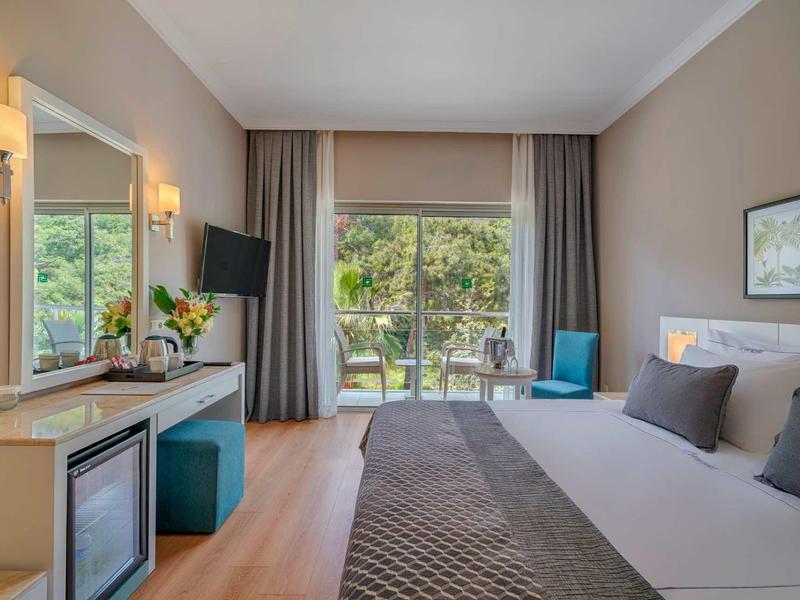 Nowoczesny pokój hotelowy z łóżkiem podwójnym, biurkiem, fotelem i widokiem na ogród.