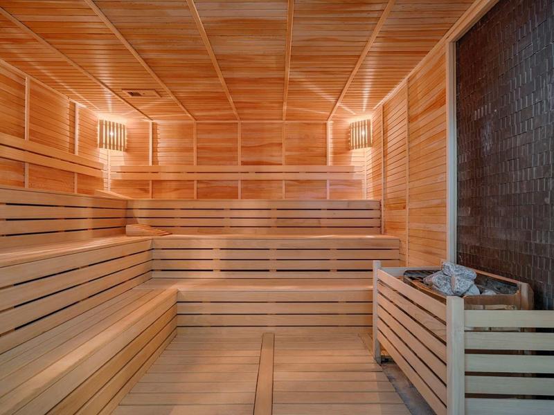 Przestronna sauna z drewnianymi ławkami i piecem na kamienie do relaksu.