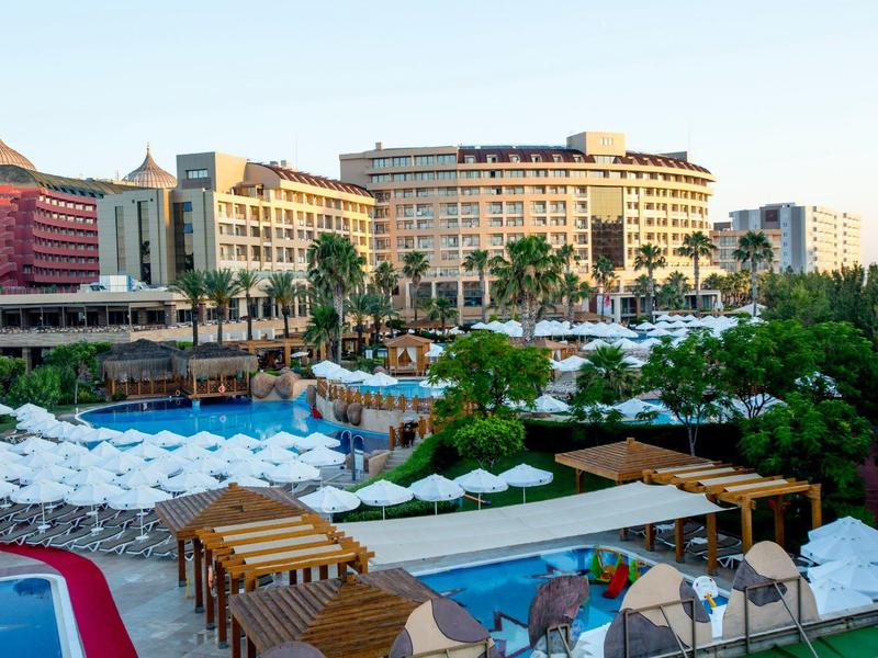 Velký hotel s několika bazény, lehátky a palmami ve slunném letovisku.