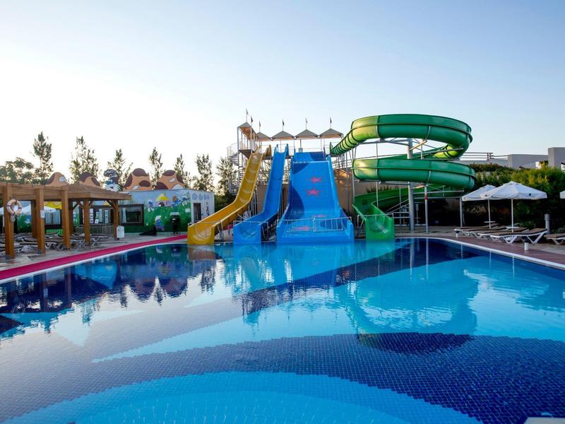 Vodní park s několika skluzavkami a čistým modrým bazénem pod slunečnou oblohou.