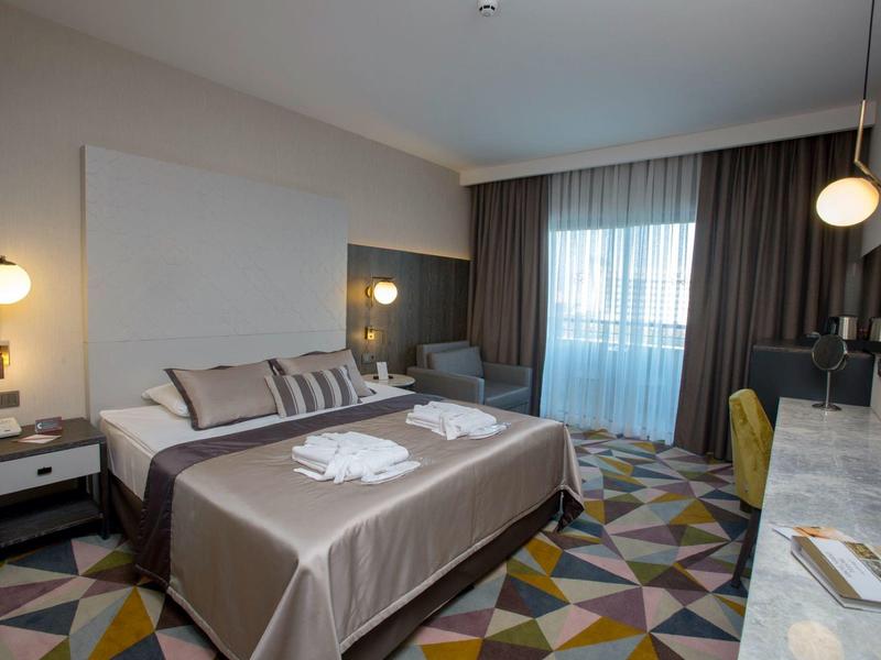 Moderně zařízený hotelový pokoj s velkou postelí, nočními stolky a oknem se závěsy.