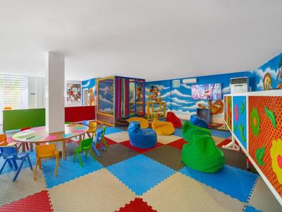Kolorowa sala zabaw z stołami, krzesłami, pufami i dziecięcymi dekoracjami ścian.