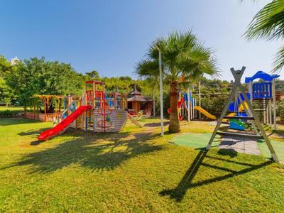 Plac zabaw z kolorowymi drabinkami, zjeżdżalniami i huśtawkami na trawie.