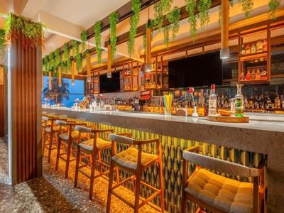 Espace bar d'hôtel moderne avec tabourets en bois, plantes et comptoir éclairé.