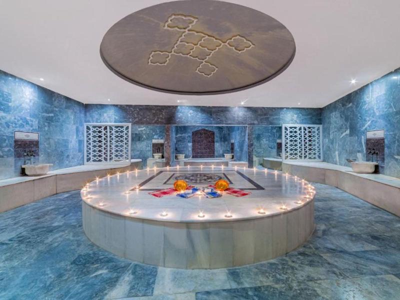 Luksusowa strefa spa z okrągłym jacuzzi, niebiesko-szarymi płytkami i oświetleniem świec.