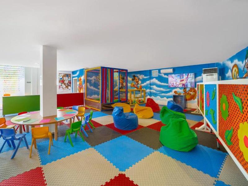Kolorowa sala zabaw z stołami, krzesłami, pufami i dziecięcymi dekoracjami ścian.