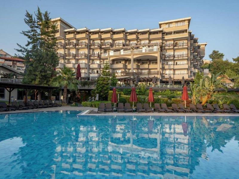 Duży budynek hotelowy wielopiętrowy z basenem na pierwszym planie pod czystym niebem.