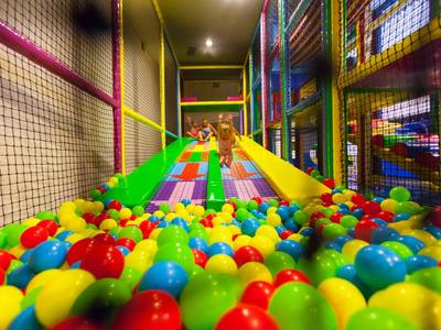 Area giochi interna per bambini con piscina di palline colorate e scivolo.