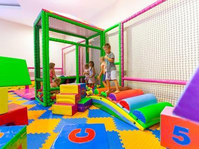 Bambini che giocano in un'area giochi interna colorata con arrampicate e tappeti.