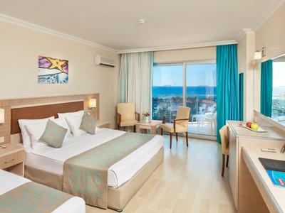 Habitación de hotel luminosa con dos camas, puerta al balcón y vista al mar a la luz del día.