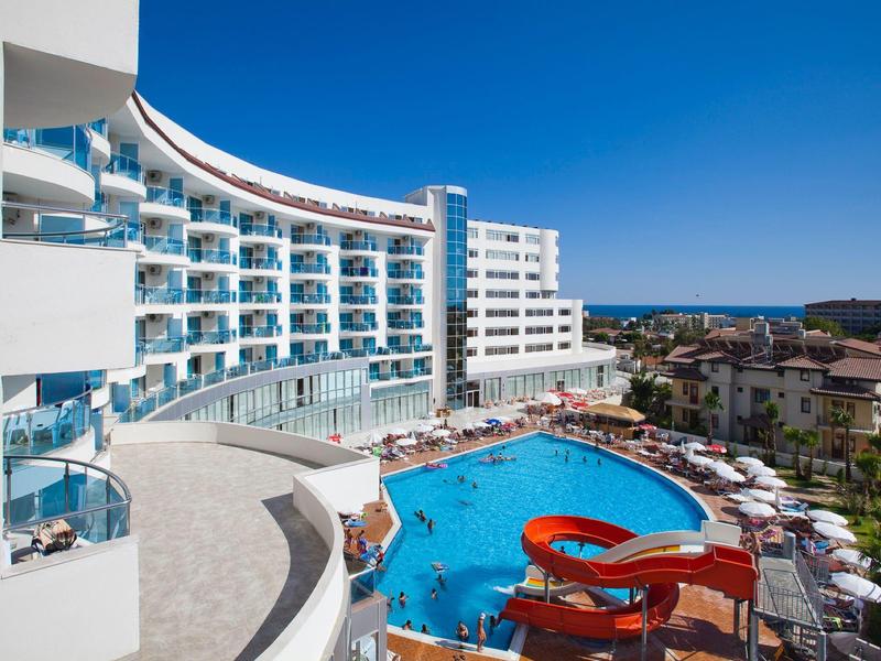 Hotel moderno con grande piscina e scivolo d'acqua rosso sotto un cielo azzurro.