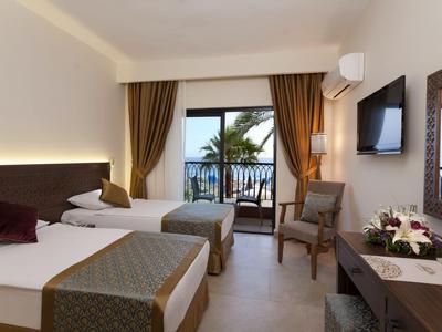 Habitación de hotel con dos camas, balcón con vistas al mar y mobiliario moderno.