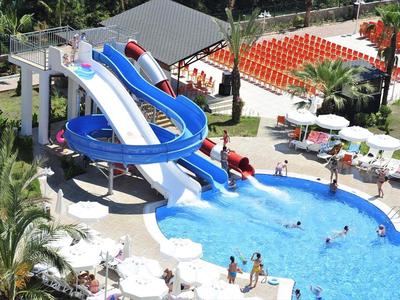 Wasserpark mit blauem Wasserrutschen und Pool, umgeben von Palmen und Liegestühlen.