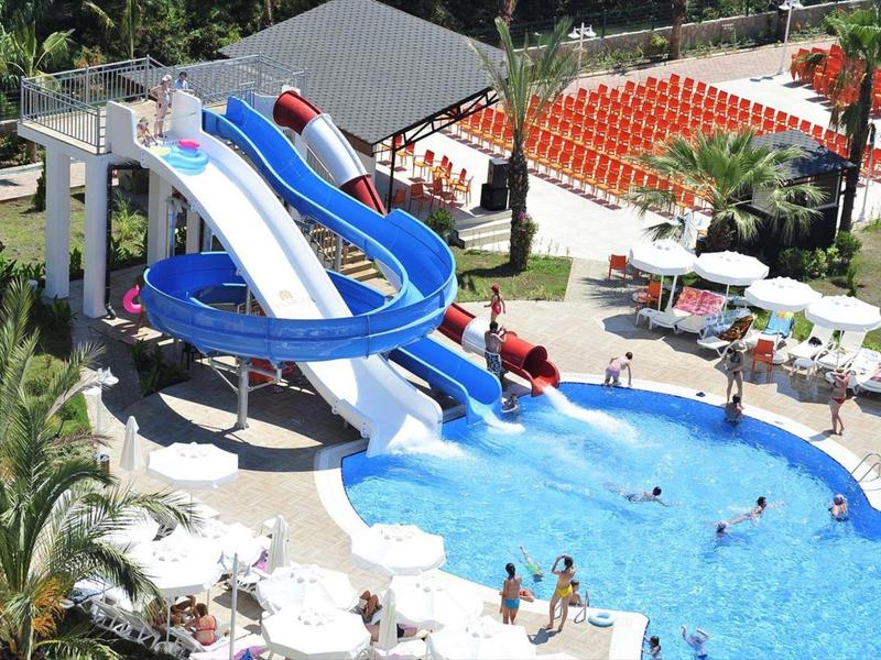 Water park with blue slides, swimmers in pool, and white lounge chairs with umbrellas nearby.