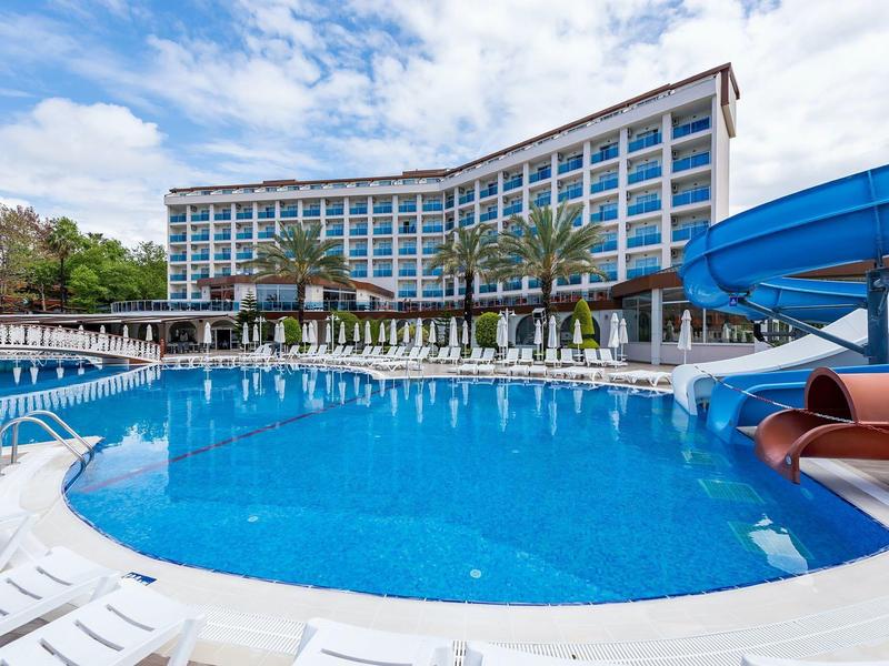 Curved hotel building with large pool, lounge chairs, and a blue water slide under blue sky.