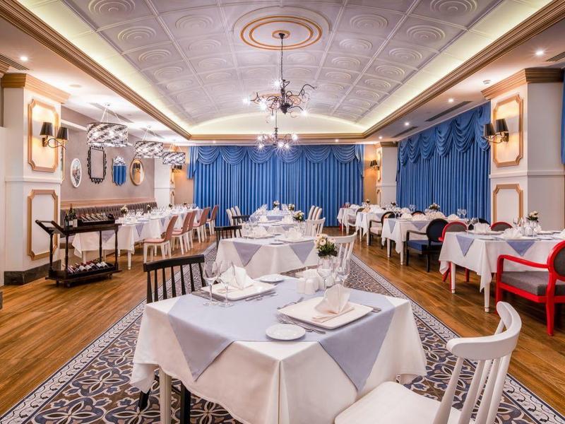 Sala da pranzo elegante con tovaglie bianche, tende blu e decorazioni classiche.