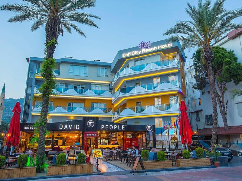 Hotel colorato su più piani con ristorante all'aperto e palme al crepuscolo.
