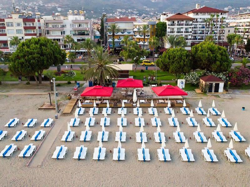 Lettini vuoti con ombrelloni rossi sulla spiaggia di sabbia davanti a una località di villeggiatura.
