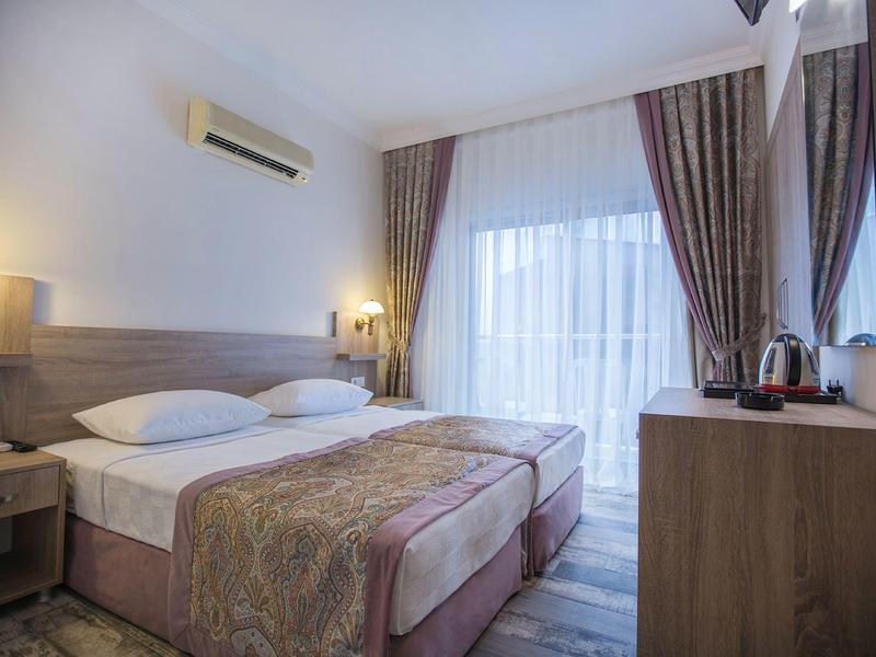 Camera d'hotel moderna con letto matrimoniale, tende chiare e mobili in legno.