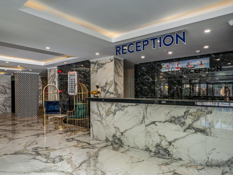 A luxury hotel lobby with a large marble reception desk and shiny marble floors.