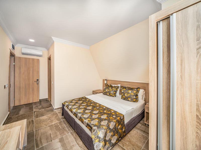 Small cozy hotel room with double bed, wooden wardrobe and neutral walls.