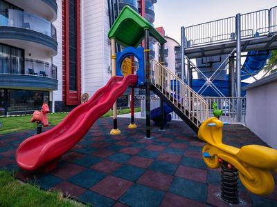 Area giochi colorata con scivolo rosso e altalene in un hotel moderno.