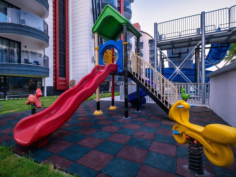 Area giochi colorata con scivolo rosso e altalene in un hotel moderno.